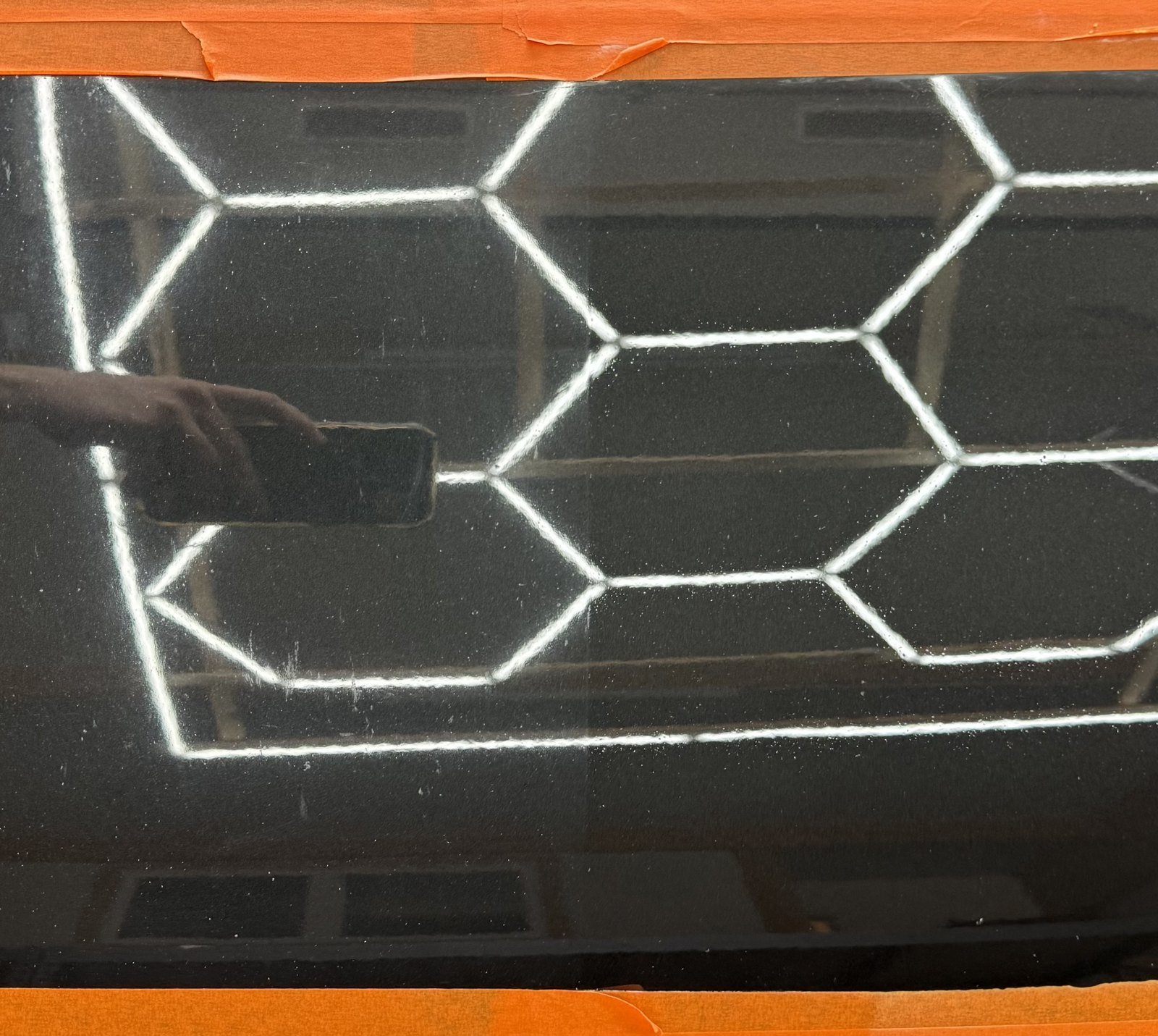 Abgeklebte schwarze Lackfläche, in der sich ein Wabenlicht spiegelt: links vor, rechts nach der Aufbereitung